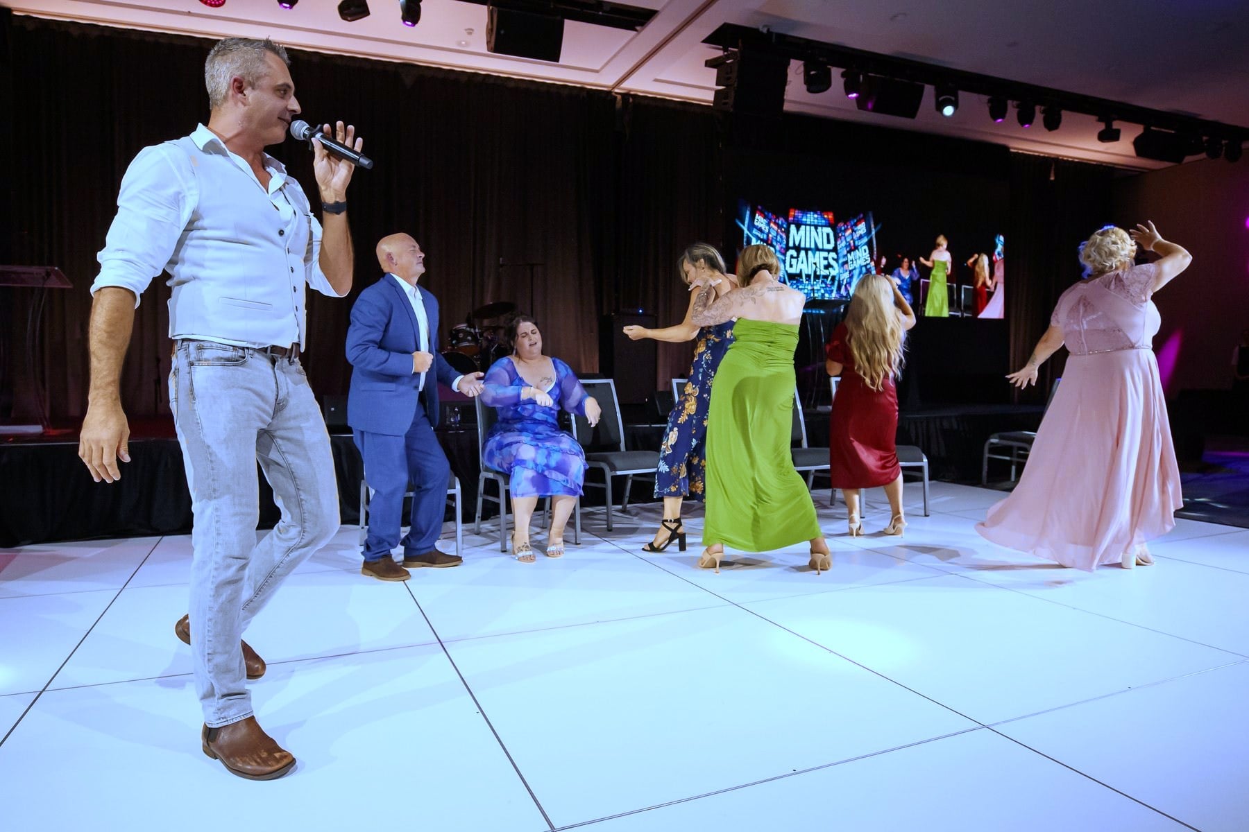 Phoenix on the microphone hosting the comedy hypnosis show at a corporate event, guests up on stage